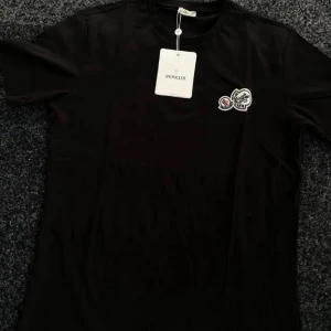 Svart t-shirt från Moncler - Snygg svart t-shirt från Moncler med ett broderat märke på bröstet. Perfekt för en stilren look. Gjord i mjukt material för extra komfort.