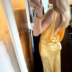 Gul balklänning - Snygg gul långklänning i satin med djup urringning och knytdetaljer där bak. Perfekt för sommarens fester och bal. Endast provad🩷