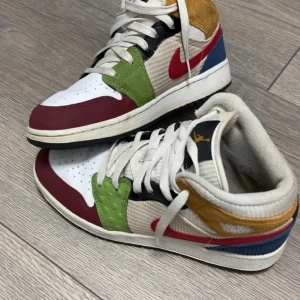 Färgglada Nike Air Jordans - Säljer ett par unika och färgglada Nike Air Jordans. Skorna har en mix av färger som röd, grön, blå, gul och vit. De är tillverkade i en kombination av material med snörning och rund tå. Perfekta för den som vill sticka ut!