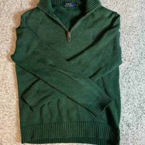 Grön stickad tröja från Polo Ralph Lauren - Säljer en snygg grön stickad tröja från Polo Ralph Lauren. Tröjan har en dragkedja vid halsen och ribbade muddar vid ärmslut och nederkant. Perfekt för kyligare dagar!