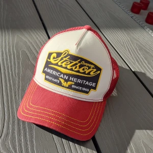 Röd och vit keps från Stetson - Snygg röd och vit keps från Stetson med ett stort märke framtill. Kepsen har en justerbar baksida i mesh för bra ventilation och komfort. Perfekt för en avslappnad stil.