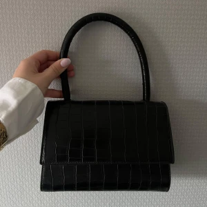 Svart handväska i krokodilmönster - Elegant svart handväska med krokodilpräglat mönster med guld detaljer.