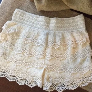Vita spets shorts - Säljer ett par vita shorts med vacker spetsdesign och elastisk midja. Perfekta för sommarens varma dagar. De har en fin volangdetalj som ger en romantisk touch. Passar bra till en avslappnad stil.