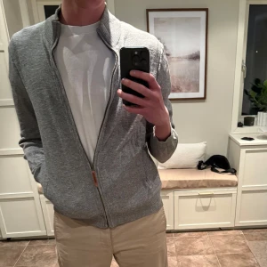 Grå stickad kofta från Fat Face - Säljer en stilren grå stickad kofta från Fat Face med dragkedja och hög krage. Perfekt för kyliga dagar och enkel att matcha med olika outfits. Passar både till vardag och mer avslappnade tillfällen.