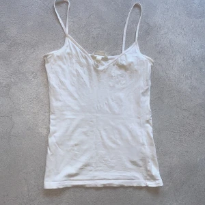Vit linnetopp - Säljer en söt vit linnetopp med smala axelband. Perfekt för varma sommardagar eller som ett basplagg i garderoben. Toppen har en enkel och stilren design.