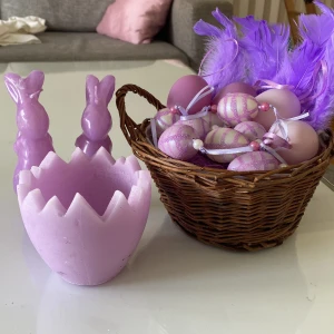 Påskdekorationer i lila - Charmiga påskdekorationer i lila, inklusive två kaninformade ljus, en korg med fjädrar och dekorerade ägg samt en äggformad ljushållare. Perfekt för att skapa en festlig stämning under påsken. Tillbehören är ej använda, fjädrarna är helt nya. Pris kan diskuteras!