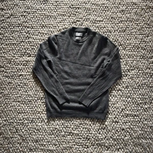 Grå merinoull tröja från Volt - Säljer en stilren grå stickad tröja från Volt. Tröjan har en klassisk rund hals och långa ärmar, perfekt för sommar kvällar. Den är mjuk och bekväm, idealisk för både vardag och avslappnade tillfällen. Pris kan diskuteras