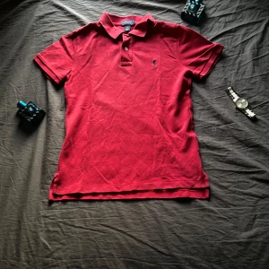 Röd pikétröja från Ralph Lauren - Säljer en snygg röd pikétröja från Ralph Lauren. Tröjan har en klassisk krage med knappar och det ikoniska broderade logotypen på bröstet. Perfekt för en stilren look.