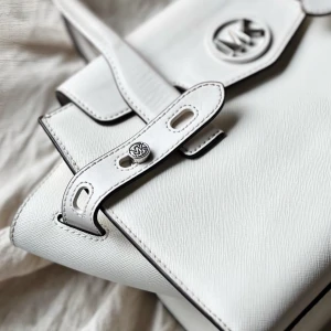 Vit handväska Michael Kors - Vit handväska från Michael Kors i perfekt skick och knappt snvänd. Silver detaljer och både handtag och justerbar axelrem. Knappt använd, köpt för länge sedan men inte använd mycket alls. Köpt för runt 2,000/3,000kr. Medium/stor, rymmer mycket