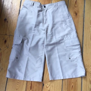 Beige cargoshorts - Säljer ett par beige cargoshorts med flera praktiska fickor och knappstängning. Perfekta för en avslappnad stil.
