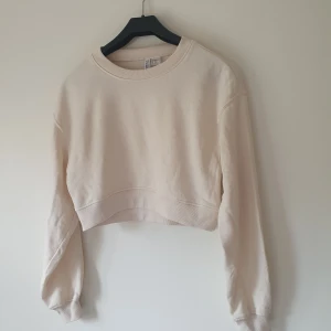 Beige croppad sweatshirt från H&M Divided - Säljer en beige croppad sweatshirt från H&M Divided. Tröjan har rund halsringning, långa ärmar och ribbade muddar. Perfekt för dig som gillar en enkel och clean stil med en modern twist. Materialet är mjuk bomullsmix som känns skön mot huden.  Helt skick dock små noppror
