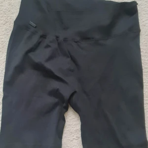 Svarta sport shorts från NOUN - Svarta shorts från NOUN i storlek L/XL. De är ribbade och har en hög midja för extra komfort. Tillverkade i en mix av polyamid, polyester och elastan som ger stretch och en tight passform. Perfekta för en chill och sportig look.