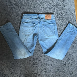 Ljusblå jeans Jack & Jones 30/32 - Säljer ett par ljusblå jeans från Jack & Jones i klassisk femficksmodell. Jeansen har normal passform, raka ben och snyggt slitna detaljer framtill. Tillverkade i bomull med en skön jeanskänsla. Perfekta för dig som gillar en avslappnad stil.