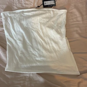 Vit ribbad tubtopp från Pieces XL - Säljer en fräsch vit ribbad tubtopp från Pieces i storlek XL. Toppen är axelbandslös och har en stilren bandeau-form. Perfekt för varma dagar och enkel att matcha med allt. Materialet är mjukt och stretchigt för en bekväm passform.