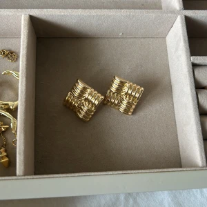 Fyrkantiga guldiga örhängen - Säljer ett par unika fyrkantiga örhängen i guldig metall med coolt ribbat mönster. De har en chunky känsla och sticker verkligen ut med sin geometriska design. Perfekta för dig som vill ha något annorlunda och trendigt i smyckeskrinet.