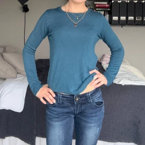 Blå långärmad stickad tröja - En enkel och stilren blå stickad tröja med rund halsringning och långa ärmar. Tröjan har en smal passform och är perfekt att matcha med jeans eller kjol. Mjuk och skön mot huden, passar dig som gillar en clean och klassisk look.