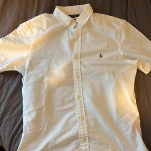 Vit kortärmad skjorta Polo Ralph Lauren - Vit kortärmad skjorta från Polo Ralph Lauren i slim fit-modell. Klassisk button-down krage och broderad logga på bröstet. Skjortan är tillverkad i bomull och har knäppning framtill. Perfekt för en clean och stilren look. Använd 1 gång 