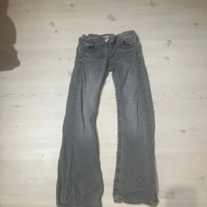 Grå bootcut jeans med fickdetaljer - Säljer ett par grå jeans med bootcut-modell och snygga fickdetaljer både fram och bak. Jeansen har klassisk femficksdesign och knappgylf. Perfekta för dig som gillar en avslappnad men ändå trendig look.