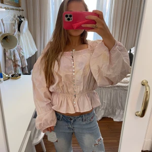 Ljusrosa blus med volang och knappar - Superfin blus med knappar i rosa och gult med stora armar. 