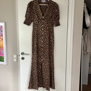 Leopardmönstrad långklänning liknande Adoore - Snygg långklänning från never fully dressed, påminner om en Adoore klänning med leopardmönster i brunt och svart. Klänningen har v-ringning, puffiga korta ärmar och knappar framtill. Den är använd 3/4 ggr så i väldigt fint skick. Nypris 1200kr