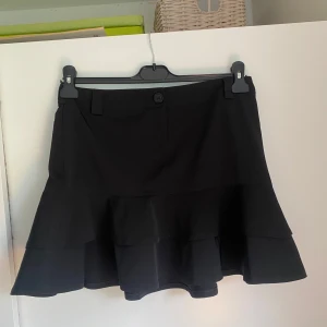 Svart minikjol med volanger  - Svart minikjol med volanger från Zoul i storlek 38. Fint skick!