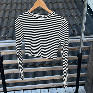 Randig croppad tröja från NA-KD - Säljer en svartvit randig croppad tröja från NA-KD i storlek S. Tröjan har långa ärmar, rund halsringning och är ribbad i materialet. Perfekt för dig som gillar en enkel men trendig stil.