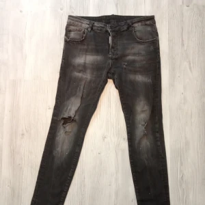Svarta skinny jeans från Dsquared2 - Säljer ett par svarta skinny jeans från Dsquared2 med slitningar och hål på benen för en riktigt edgy look. Jeansen har klassisk femficksdesign, snygg Dsquared2-patch bak och är tillverkade i stretchig bomull för skön passform.
