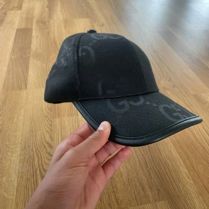Svart Jumbo keps - Snygg svart keps med GG-logga i mönstret över hela kepsen. Klassisk böjd skärm och justerbar passform. Perfekt accessoar för en trendig look.