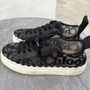 Svarta sneakers från Chloé med spets -  svarta sneakers från Chloé med spetsdetaljer och  vit sula. Skorna har snörning, genomskinliga meshpartier och stor logga baktill. I storlek 38 