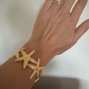 Guldigt armband med sjöstjärnor - Unikt armband i guldton med stora sjöstjärneformade detaljer som ger en cool strandkänsla. Armbandet är i metall och har en iögonfallande design som verkligen sticker ut. Perfekt för dig som vill ha något annorlunda och trendigt.