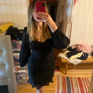 Svart kort klänning från Nelly - Supersnygg svart kort klänning från Nelly med puffiga långärmar och rynkade detaljer över hela klänningen. Sitter figurnära. 