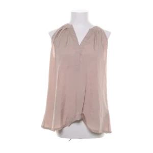 Beige blus med skimmer - Säljer en beige blus från Gina Tricot i lätt och flowy polyester. Toppen har v-ringning, är ärmlös och har en avslappnad passform med fina rynkade detaljer vid axlarna. Perfekt för dig som gillar stilrena och enkla plagg.