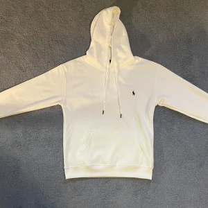 Vit hoodie från Polo Ralph Lauren - Snygg vit hoodie från Polo Ralph Lauren med klassisk broderad logga på bröstet. Tröjan har huva med snörning, känguruficka och långa ärmar. 
