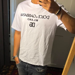 Vit Dolce & Gabbana t-shirt - Säljer en vit t-shirt från Dolce & Gabbana med svart broderad logga och texten 'Milano' på bröstet. Klassisk rund halsringning och korta ärmar. Skön passform och tillverkad i mjuk bomull. Perfekt för dig som gillar stilrena designer med exklusiv känsla.