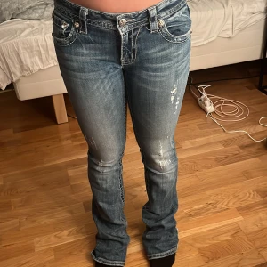 Miss Me bootcut jeans med broderi - Snygga blå bootcut jeans från Miss Me i storlek 27. Jeansen har slitningar framtill och coola bakfickor med broderade detaljer och nitar. Klassisk femficksmodell med låg midja och kontrastsömmar. Perfekta för dig som gillar statement-jeans!