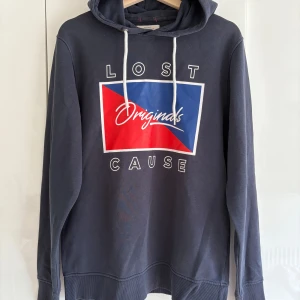 Mörkblå hoodie Jack & Jones  - Säljer en mörkblå hoodie från Jack & Jones Originals med vit snörning och tryck i rött, blått och vitt på bröstet. Tröjan har huva och långa ärmar. Storlek L (men skulle säga att den är lite liten i storleken, mer som medium, eller tajt large)