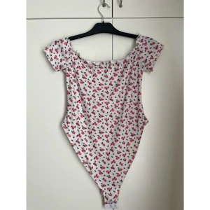 🌸 Blommig off-shoulder bodysuit från SHEIN – Strl M/L (EU 40/42) 🌸 - 🌸 Blommig off-shoulder bodysuit från SHEIN – Strl M/L (EU 40/42) 🌸   Säljer en superfin och feminin bodysuit från SHEIN med ribbat tyg och ett romantiskt blommönster i rosa/rött och grönt mot vit bakgrund. Bodyn har en bardotringning (off-shoulder) med volangkant och söta puffärmar – perfekt för en somrig, söt och stilren look!  Perfekt att matcha med jeans, kjol eller shorts till både vardag, utekvällar och somriga tillfällen.  ✅ Sparsamt använd ✅ Mycket gott skick ✅ Skön stretchig passform
