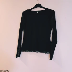 Svart meshblus med volangkant från HPO woman strl 38/40 - Svart transparent meshblus från H&M med långa ärmar och volangkant vid ärmslut och nederkant. Blusen har en figurnära passform och är perfekt för att skapa en cool lager-på-lager-look. Tunn och luftig, passar till många olika stilar.  Helt & fint skick