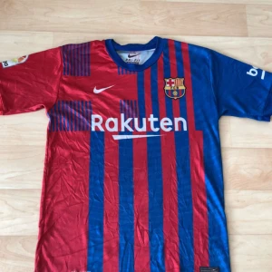 FC Barcelona Pedri matchtröja Nike - Säljer en officiell FC Barcelona matchtröja med Pedri #16 på ryggen. Tröjan är kortärmad, har klassiska blå och röda ränder, klubbmärke på bröstet, La Liga-märke på ärmen och Rakuten som sponsor. Tillverkad i lätt och ventilerande Dri-Fit-material.