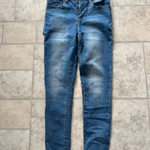 Levi's 721 High Rise Skinny Jeans - Säljer ett par Levi's 721 High Rise Skinny jeans i klassisk blå tvätt. Jeansen har hög midja, skinny fit och snygga slitningar framtill. Tillverkade i stretchig denim för en bekväm passform. Perfekta för dig som gillar en smal siluett och tidlös stil.