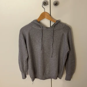 Grå hoodie med huva och snörning - En stilren grå hoodie med huva och snörning. Tröjan har långa ärmar och ribbade muddar vid ärmslut och nederkant. Perfekt för en chill och avslappnad look. Passar dig som gillar enkel och klassisk streetstyle. Storlek S/M men skulle säga att den passar XS/S. Aldrig använd.