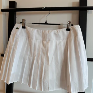 Vit plisserad kjol från Lacoste Sport - Superfräsch vit plisserad kortkjol från Lacoste Sport. Klassisk tennisstil med snygga veck och diskret Lacoste-logga framtill. Perfekt för dig som gillar sportig och clean look. Kjolen är gjord i ett lätt och bekvämt material.