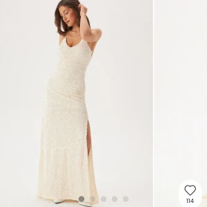 Glittrig långklänning i champagne - Supersnygg långklänning i champagnefärg med glittriga paljetter över hela tyget. Klänningen har smala axelband, v-ringning och en hög slits på sidan. Perfekt för bal eller nyår, ger en riktigt lyxig känsla och sticker ut i mängden.