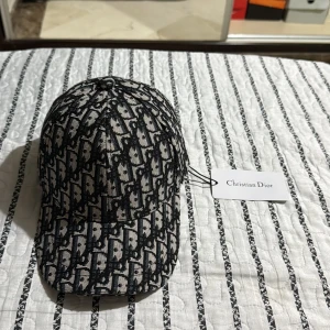 Christian Dior monogram keps - Snygg keps från Christian Dior med ikoniskt svart och vitt monogrammönster. Kepsen har böjd skärm, justerbar rem med gulddetalj med text. Perfekt för dig som vill sticka ut med lyxig streetstyle.sällsynt och bra material och kvalitet. Kom dm för frågor och funderingar!