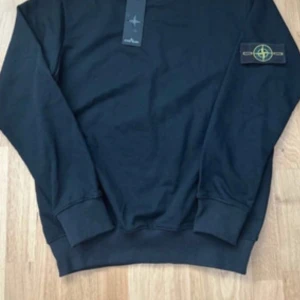 Svart sweatshirt från Stone Island - Snygg svart sweatshirt från Stone Island med klassisk patch på ärmen. Tröjan har rund hals, långa ärmar och ribbade muddar. Perfekt för dig som gillar stilrena och trendiga plagg med streetkänsla.