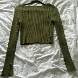 Olivgrön ribbad tröja med hög krage - Snygg olivgrön tröja med ribbat stickat material och långa ärmar. Ärmarna har en slitsdetalj vid mudden. Den har en båtturingning. Så himla lyxigt material då den är ganska tjock i tyget🤩