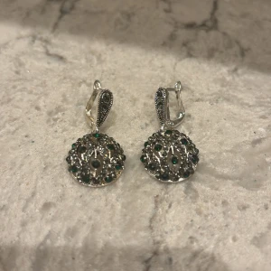 Silverörhängen med gröna stenar - Eleganta silverörhängen med rund design och gröna stenar. Detaljerade mönster ger en vintagekänsla. Perfekta för att ge en touch av glamour.