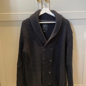 Stickad kofta  - Säljer en mysig grå stickad kofta med dubbelknäppning och bred krage. Perfekt för kyliga dagar. Koftan har långa ärmar och en strukturerad stickning. Köpt helt ny för 4500kr men svår såld så därför priset.