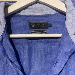 Blå skjorta från Riley - Snygg blå skjorta från Riley i slim fit. Skjortan har långa ärmar och knappar framtill. Perfekt för en stilren look. Kolla gärna in min profil då jag rensar ut hemma och lägger ut mycket nu. Vid köp av flera artiklar kan rabatt ges!