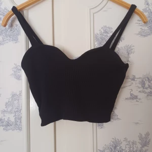 Svart ribbad korsettopp - Snygg svart ribbad korsettopp med dubbla axelband. Perfekt för en stilren look. Toppen är croppad och har en figurnära passform.